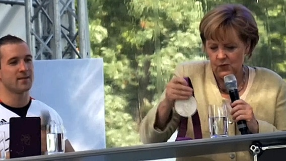 Angela Merkel betrachtet eine Medaille © Screenshot 