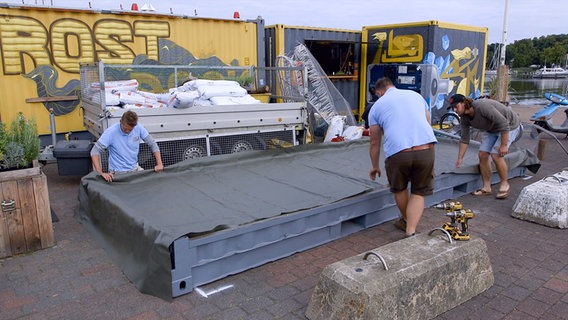 Die Garten-Docs legen eine Teichplane über eine ehemalige Bodenplatte eines Schiffscontainers. © NDR/nonfiction planet 