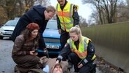 Gleiche Stelle, gleiches Auto, wieder ein Montag: Lukas Petersen (Patrick Abozen, 2.v.r.) und Jessy (Farina Flebbe, r.) wollen einen eigentlich harmlosen Auffahrunfall zwischen den Halbbrüdern Roderick Brüggemann (Uke Bosse,2.v.l.) und Guido Schneider (Andreas Birkner, liegend) aufnehmen, dabei wird Guido Schneider überfahren. Schneiders Verlobte Sherin Noury (Leila Abdullah, l.) ist entsetzt. © NDR/ARD/Cornelia Klein 
