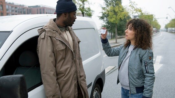 Harry Möller (Maria Ketikidou, r.) kontrolliert Edson Nuambe (Ibrahima Sanogo, l.), der eine rote Ampel überfahren hat. Der Schwarzafrikaner hat sich einen Van der Großschlachterei Dittmer, in der er illegal arbeitet, geschnappt, um zu seiner hochschwangeren Frau zu kommen. © NDR/ARD/Thorsten Jander 