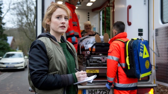 Nina Sieveking (Wanda Perdelwitz, l.) überwacht den Abtransport des Rentners Martin Schropp (Michael von Rospatt, im HG). Er hat einen Einbrecher in seiner Wohnung überrascht und wurde schwer verletzt.. © NDR/ARD/Thorsten Jander 