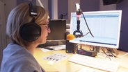 Eine Frau mit Kopfhörern vor einem Mikrofon  