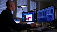 Ein Mann sitzt vor einem Computer-Bildschirmen, auf denen eine Grafik und Zahlen zu sehen sind. © Screenshot 