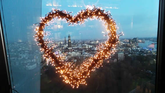 Ein Herz aus kleinen Lämpchen hängt an einem Fenster. Durch das Herz ist in weiter Ferne der Hamburger Michel zu sehen. © Enno Marfeld Foto: Enno Marfeld
