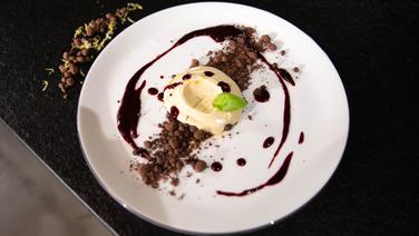 Flüssiger Käsekuchen mit Schokoladen-Erde und Beeren-Püree auf einem Teller serviert. © NDR/Doclights GmbH 