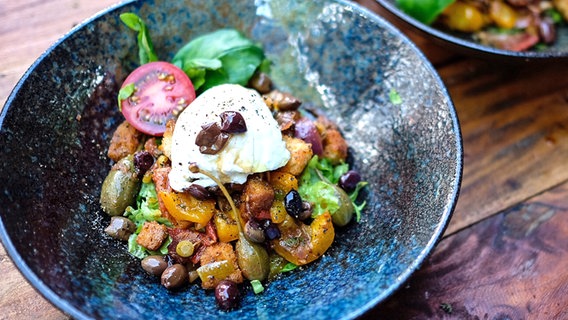 Brotsalat mit Paprika, Tomaten, Kapernäpfel und italienischem Frischkäse sowie Salat auf einem tiefen Teller serviert © NDR 