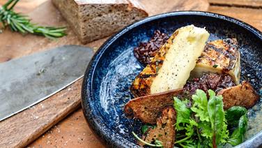 Karamellisierter Käse mit Feigen-Zwiebel-Chutney, Salat und gerösteten Brotscheiben auf einem Teller © NDR 