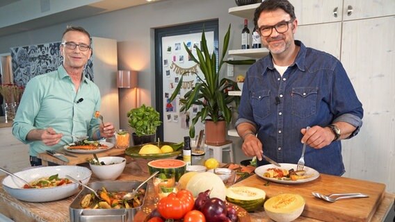 Fernsehkoch Tarik Rose (rechts) und Ernährungsmediziner Dr. Matthias Riedl stehen in einer Küche und essen Antipasti. © NDR Foto: Florian Kruck