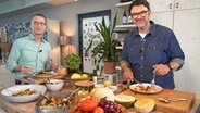 Fernsehkoch Tarik Rose (rechts) und Ernährungsmediziner Dr. Matthias Riedl stehen in einer Küche und essen Antipasti. © NDR Foto: Florian Kruck