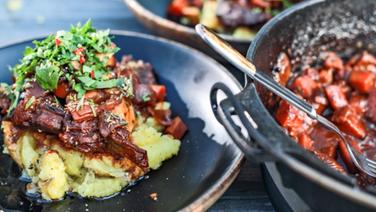 Ossobuco vom Auerochsen auf Kartoffelstampf und Gemüse in einer dunklen Schüssel serviert. © NDR Foto: Tarik Rose