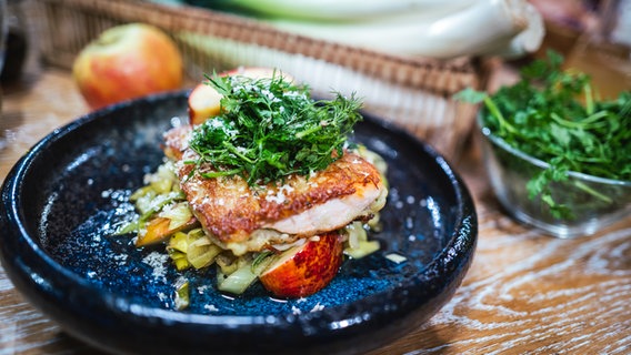 Fischfilet im Kartoffelmantel mit Apfel-Lauchgemüse auf einem Teller angerichtet. © NDR Foto: Tarik Rose