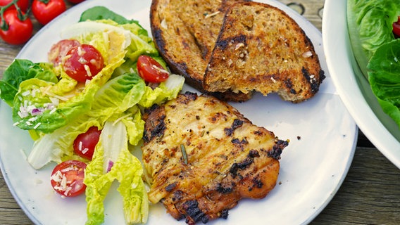 Grilled chicken served on a plate with Caesar salad and toast.  © NDR Photo: Florian Kruck