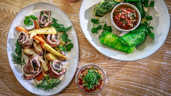 Auf einem Tisch stehen ein Teller mit Sommerrollen, einer mit Rouladen und Ofengemüse sowie ein Schälchen mit Himbeer-Kokoscreme. © NDR Foto: Tarik Rose