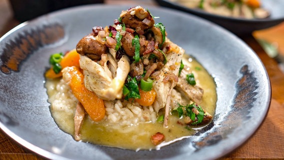 Weißwein-Huhn auf Risotto mit Speck-Champignons auf einem Teller serviert. © NDR 