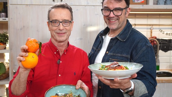 Tarik Rose und Dr. Matthias Riedl halten zwei Teller mit gesunden Gerichten in die Kamera. © NDR/dmfilm/Florian Kruck 