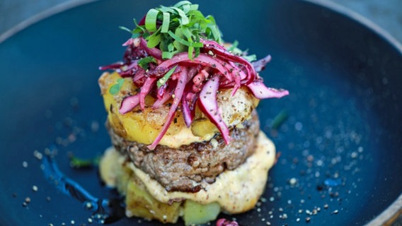 Ein Burger mit Kartoffeln, Rotkohlsalat und Mayonnaise auf einem tiefen Teller serviert. © NDR Foto: Tarik Rose