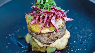 Ein Burger mit Kartoffeln, Rotkohlsalat und Mayonnaise auf einem tiefen Teller serviert. © NDR Foto: Tarik Rose