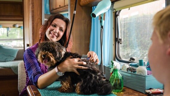 Szenenbild aus der Comedy-Serie "Jennifer - Sehnsucht nach was Besseres": Jennifer frisiert einen Hund in ihrem Hundesalon, einem alten Wohnwagen. © NDR/Marion von der Mehden 