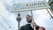 Michel Abdollahi mit einem Schild mit der Aufschrift Euros nach Athen tragen!  