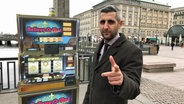 Michel Abdollahi steht auf dem Hamburger Rathausmarkt und zeigt mit dem Finger in die Kamera. © NDR / Stefan Mühlenhoff 