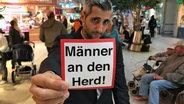 Michel Abdollahi hält ein Schild in der Hand: Männer an den Herd! © NDR / Stefan Mühlenhoff 