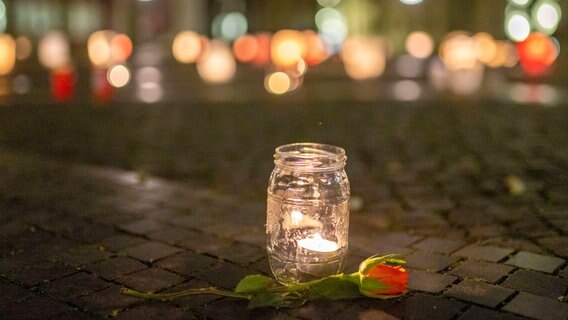 Eine Kerze und eine Rose liegen auf einem gepflasterten Gehweg. © mago images/Hoch Zwei Stock/Angerer 