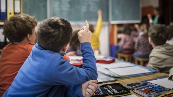 Junge Schüler sitzen an Tischen und blicken zur Tafel © imago/photothek 