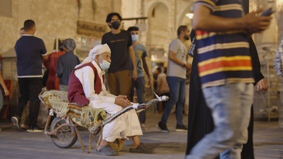 Ein alter Mann sitzt in Katar in einer Schubkarre auf einer Decke. © NDR 