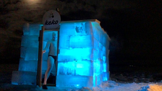 Ein Mann verlässt im Dunkeln die von innen beleuchtete Eis-Sauna in Lappland. © NDR/Florianfilm 