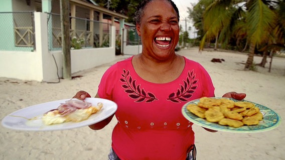 Mireya hält Teller mit Kochbananen in der Hand. Sie lacht. © NDR/docstation/Marco Berger 