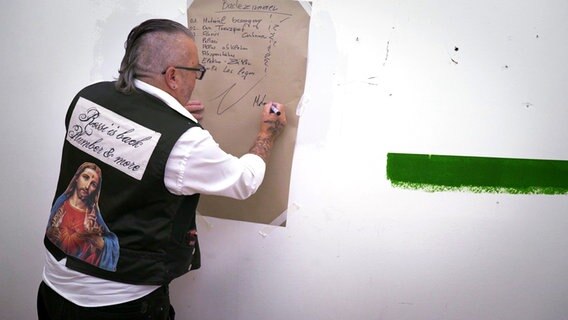 Ein Mann hat sich eine Liste mit geplanten Arbeiten an die Wand gehängt. © NDR/nonfictionplanet 