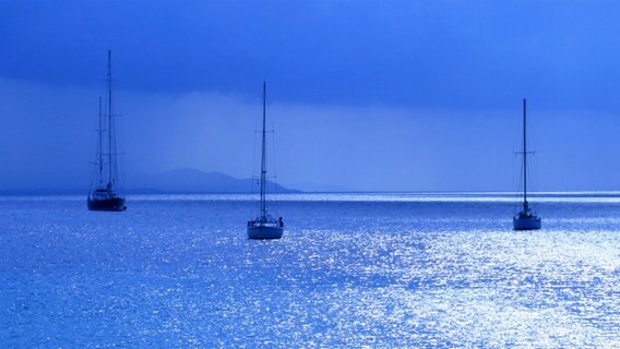 Segelboote in der blauen Stunde auf glitzerndem Wasser vor Sardinien. © NDR Foto: Wilfried Nagel