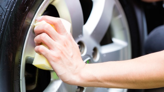 Ein Mann reinigt die Felgen eines Autos mit der Hand. © Colourbox Foto:  Kzenon