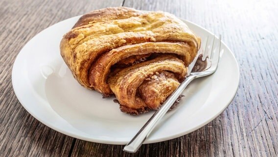 Ein Franzbrötchen liegt auf einem weißen Teller mit einer Kuchengabel. © Colourbox Foto: -