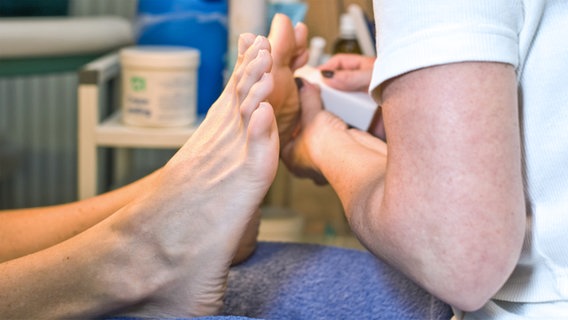 Eine Fußpflegerin behandelt die Füße eines Kunden. © Dron/fotolia Foto: Dron