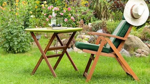 Ein Gartentisch und -stuhl aus Holz stehen auf dem Rasen in einem sommerlichen Garten. © Fotolia.com Foto: K.-U. Häßler