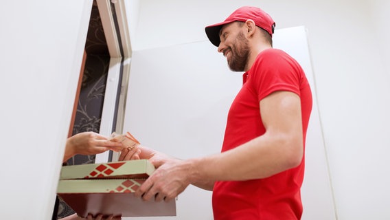 Ein Lieferant übergibt Pizzaschachteln an der Haustür. © Colourbox Foto: Syda Productions