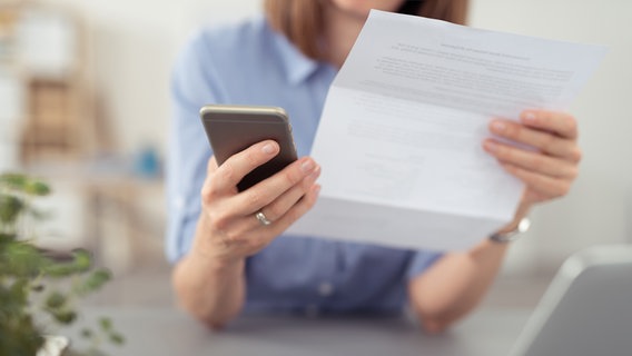 Eine Frau liest eine Rechnung mit einem Smartphone in der Hand. © Fotolia Foto: contrastwerkstatt
