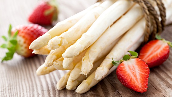 Ein Bund weißer Spargel auf einem Holztisch, daneben liegen ein paar Erdbeeren. © Fotolia.com Foto: Corinna Gissemann