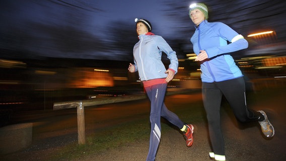 Zwei junge Frauen joggen in der Abenddämmerung im Winter mit Stirnlampen. © picture alliance / imageBROKER Foto: Jochen Tack