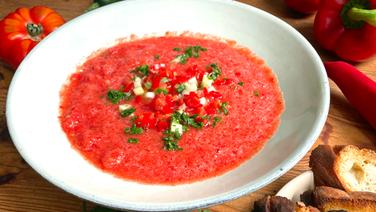 Die kalte Tomatensuppe Gazpacho mit Kräutern in einem tiefem Teller serviert. Daneben liegt Gemüse und geröstetes Brot. © NDR 