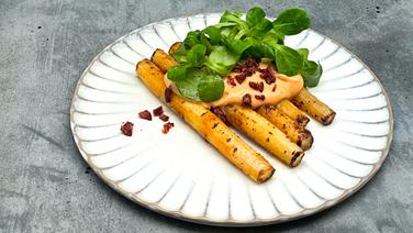 Black salsify with hollandaise sauce, cranberries and lamb's lettuce on a white plate.  © NDR 