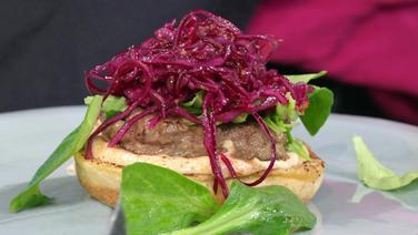 Wildburger mit Rotkohl-Salat auf einem Teller serviert. © NDR 