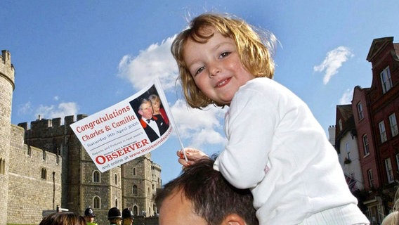 9. April 2005: Am Hochzeitstag von Camilla und Charles sitzt ein kleines Mädchen auf den Schultern ihres Vaters und hat eine Fahne in der Hand © Picture-Alliance / dpa Foto: Fiona Hanson