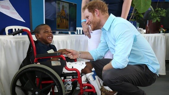 Prinz Harry begrüßt ein Kind im Rollstuhl bei seinem Besuch auf der Karibik-Insel St. Lucia. © picture alliance / empics Foto: Chris Radburn