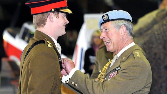Lächelnd nimmt Prinz Harry am 7. Mai 2010 das zur bestandenen Pilotenausbildung gehörende Abzeichen von seinem Vater, Prinz Charles, entgegen. © picture alliance / dpa 