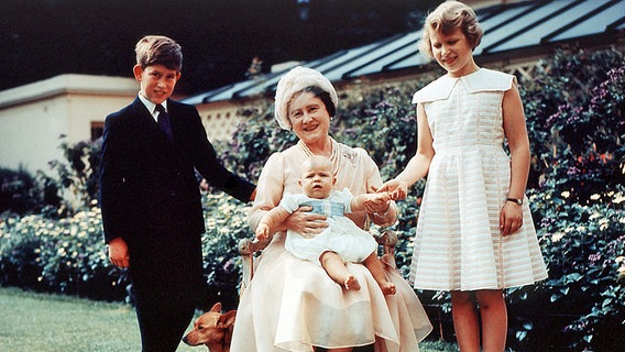 Mit ihren Enkeln Prinz Charles, Prinzessin Anne und Prinz Andrew (auf ihrem Schoß), sitzt die britische Königinmutter Elizabeth 1960 auf einer Gartenbank. © dpa - Fotoreport 