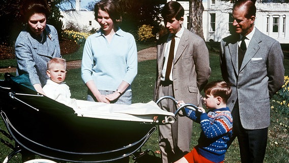 1965: Königin Elizabeth, Prinzessin Anne, Kronprinz Charles, Prinz Philip und Prinz Andrew blicken auf den im Kinderwagen sitzenden Prinz Edward. © Picture-Alliance / dpa / Press Association 