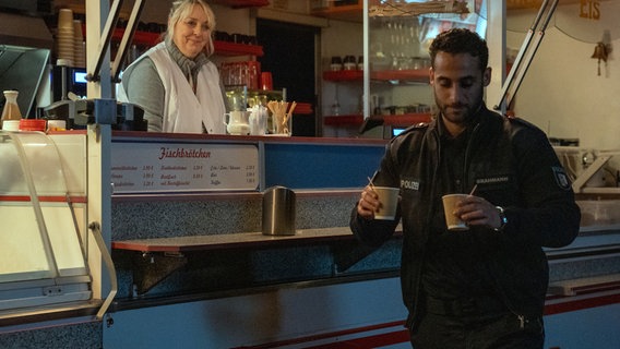Während der Nachtschicht holt Polizist Brahmann (Karim Günes, r.) Kaffee für sich und seinen Kollegen am Ibisswagen (mit Maraile Woehe, l.). Während der Nachtschicht holt Polizist Brahmann (Karim Günes, r.) Kaffee für sich und seinen Kollegen am Ibisswagen (mit Maraile Woehe, l.). © NDR/Marion von der Mehden