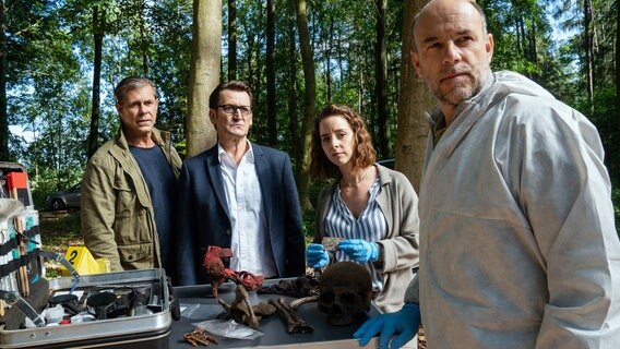 Am Fundort der Leiche werden Finn Kiesewetter (Sven Martinek, l.) und Lars Englen (Ingo Naujoks, 2.v.l.) schon von Ida Müller-Dogan (Amelie Plaas-Link, 2.v.r.) und Rechtsmediziner Dr. Henning Strahl (Christoph Tomanek, r.) empfangen. © NDR/Marion von der Mehden 